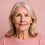 Mulher de 50 anos com expressão confiante, pele saudável e fundo rosado, representando resultados do uso contínuo de colágeno Verisol.